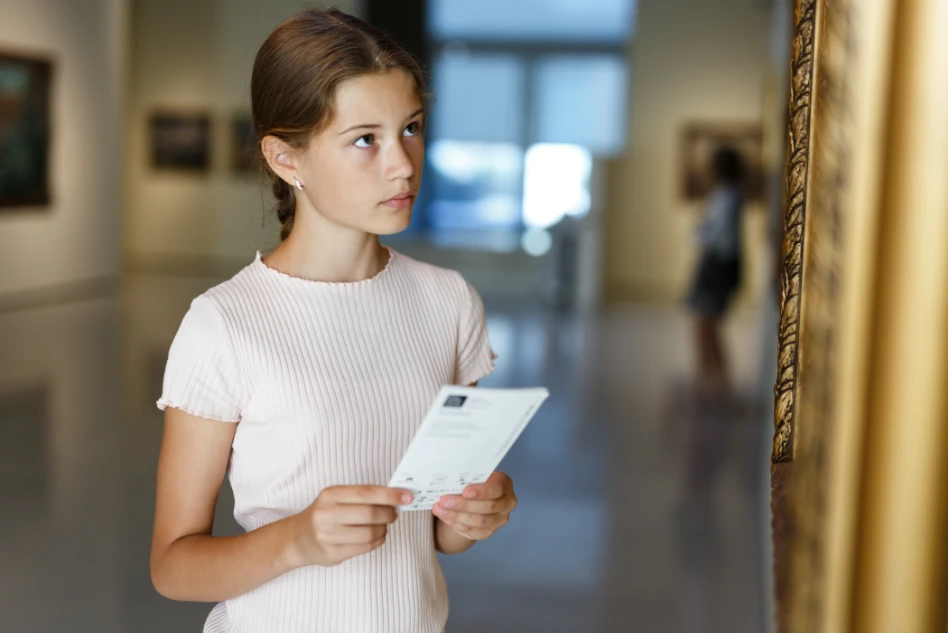 Foto di una ragazzina che osserva un dipinto in un museo con un opuscolo in mano