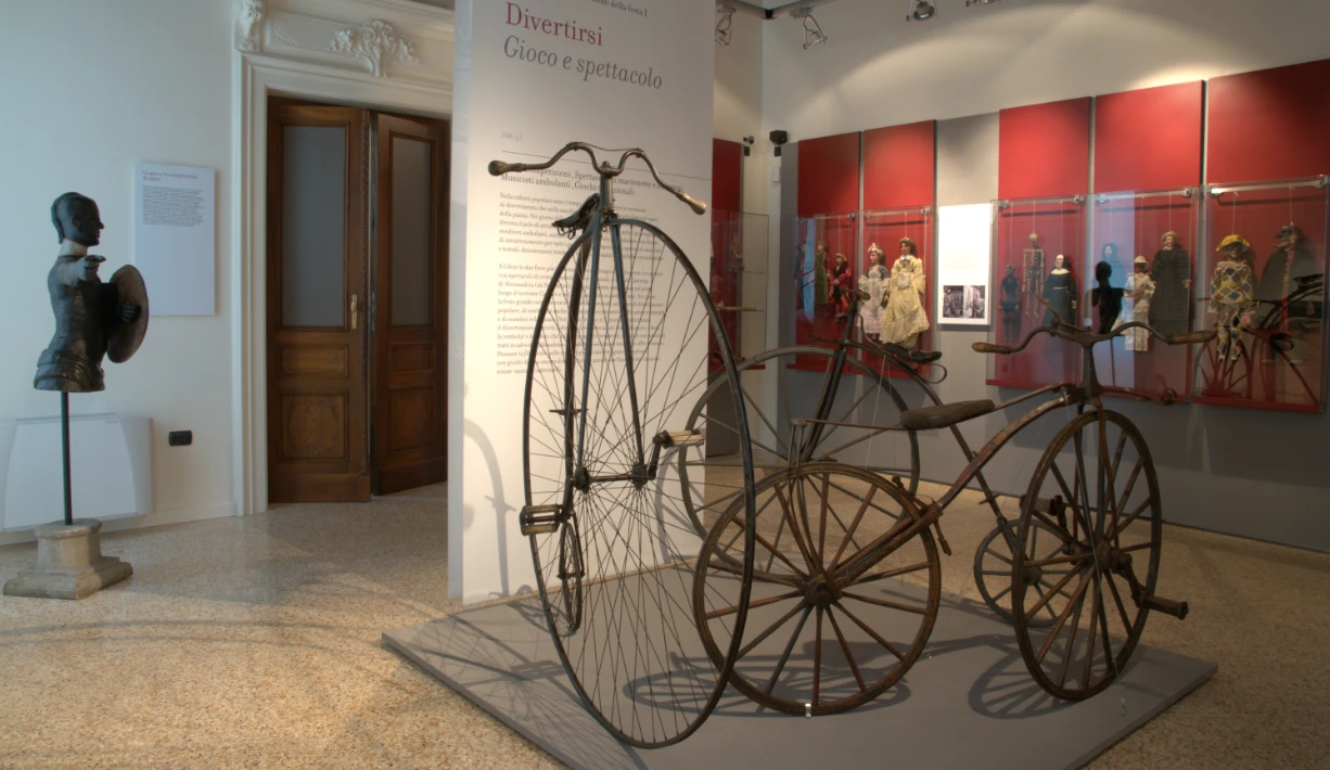 Foto della Sala dei Giochi del museo etnografico di Udine con vecchie biciclette e bambole
