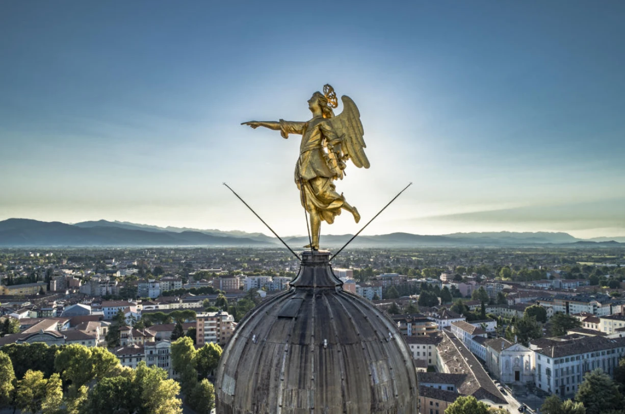 Foto della statua dell'angelo dorato di Udine posizionato sul campanile della Chiesa di Santa Maria. La città di Udine sullo sfondo.